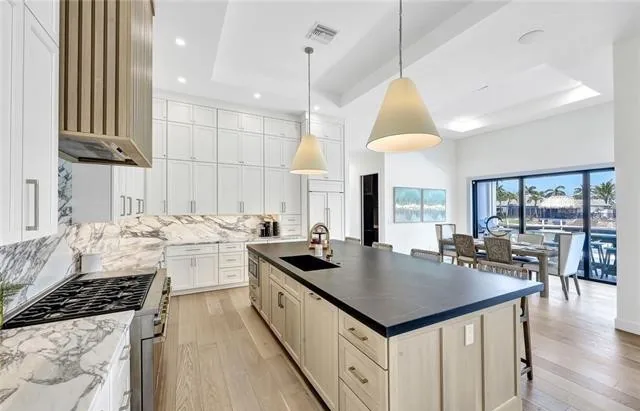 A finished kitchen with a long island, marble backsplash and a view out to the water